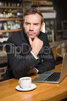 Thoughtful man using laptop and having a coffee