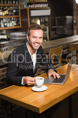 Handsome man using laptop and having a coffee