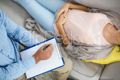 Doctor writing on clipboard while consulting pregnant woman