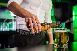 Mid section of bartender pouring beer in a glass