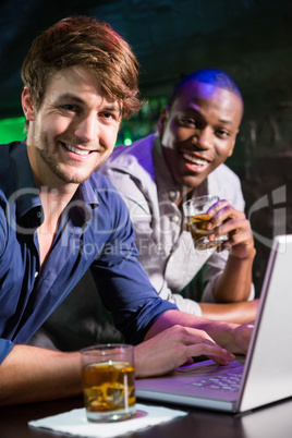 Two men having whiskey and using laptop at bar counter