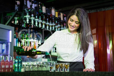 Pretty bartender pouring tequila into glasses