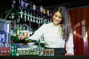 Pretty bartender pouring tequila into glasses