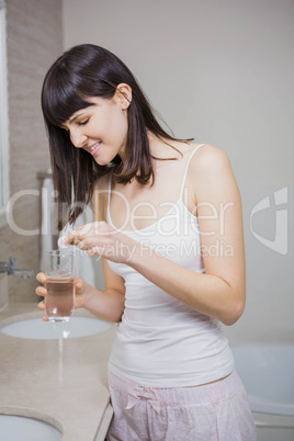 Beautiful woman putting pill in to a glass of water