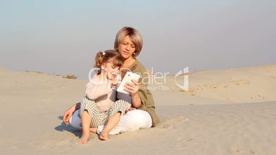 mother and daughter play with tablet in desert