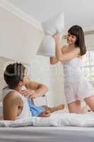 Woman playing pillow fight with man on bed