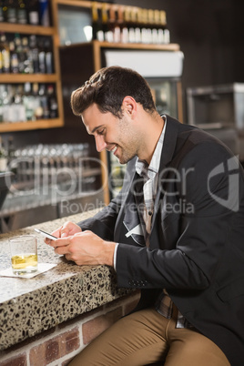 Handsome man having a whiskey and using smartphone