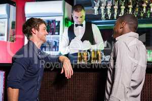 Two men smiling and talking to each other while having beer at b