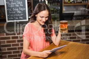 Pretty woman having a beer and looking at tablet