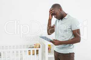 Tensed man standing next to a cradle and using digital tablet