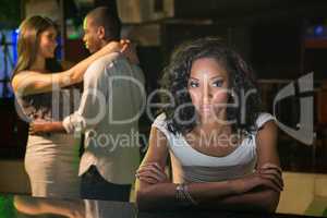 Unhappy woman sitting at bar counter and couple dancing behind h