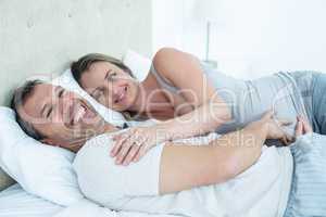 Expecting couple lying on bed and chatting