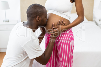 Man kissing pregnant womans belly in bedroom