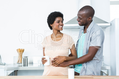 Pregnant couple embracing while having cup of coffee