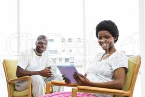 Smiling pregnant woman using digital tablet and man sitting on c