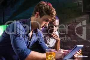 Two men having whiskey and using digital tablet at bar counter