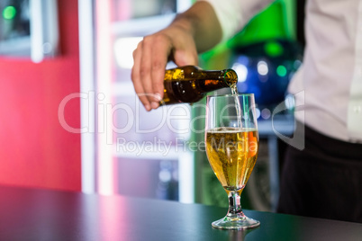 Mid section of bartender pouring beer in a glass