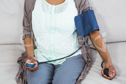 Pregnant woman checking blood pressure in living room