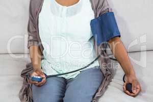 Pregnant woman checking blood pressure in living room