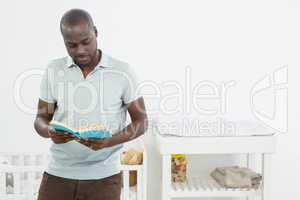 Man standing in front of a cradle and reading a book