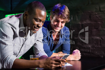 Two men looking at mobile phone and smiling at bar counter