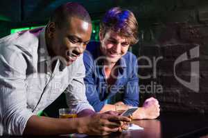 Two men looking at mobile phone and smiling at bar counter