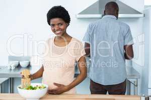 Pregnant woman preparing salad in kitchen