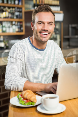 Handsome man using laptop and having a croissant