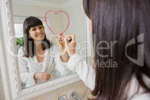 Young beautiful woman drawing big heart on mirror