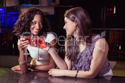 Young women toasting cocktail glasses at bar counter