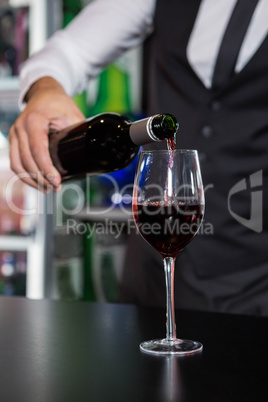 Mid section of bartender pouring red wine in a glass