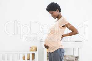 Pregnant woman standing near cradle and looking at her stomach