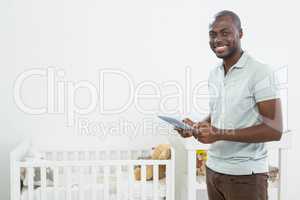 Smiling man standing next to a cradle and using digital tablet