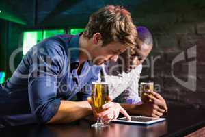 Two men using digital table while having beer at bar counter