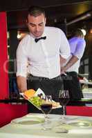 Waiter serving fruits and red wine on a table