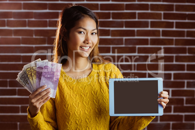Smiling asian woman showing tablet and bank notes