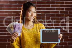 Smiling asian woman showing tablet and bank notes