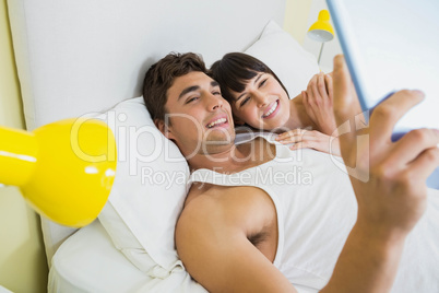 Couple using digital tablet on bed