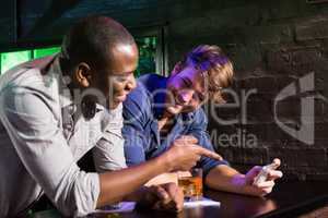 Two men looking at mobile phone and talking at bar counter