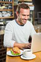 Handsome man using laptop and having a croissant