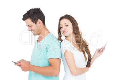 Smiling couple using their smartphones back to back