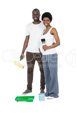 Pregnant couple holding roller paint and paint brush