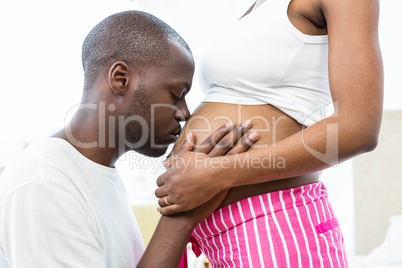 Man kissing pregnant womans belly in bedroom