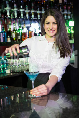 Pretty bartender pouring a blue martini drink in the glass