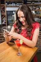 Pretty woman using her smartphone and having a cocktail