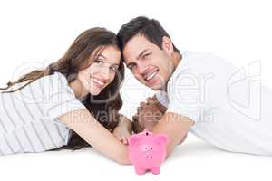 Happy couple lying on the floor with piggy bank