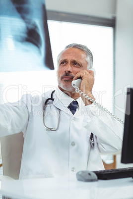 Doctor checking a x-ray report while talking on phone