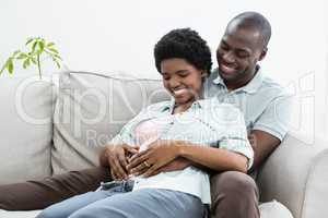 Man touching pregnant womans stomach on sofa
