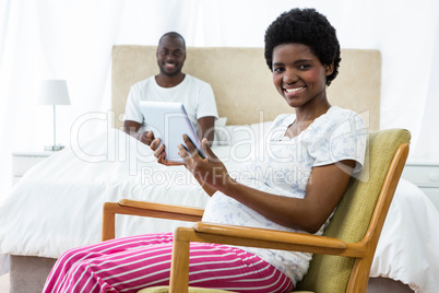 Pregnant woman using digital tablet on chair and man sitting on