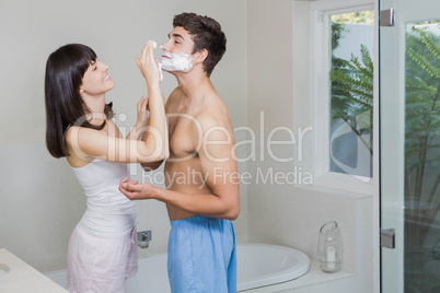 Young woman applying shaving cream on young mans face